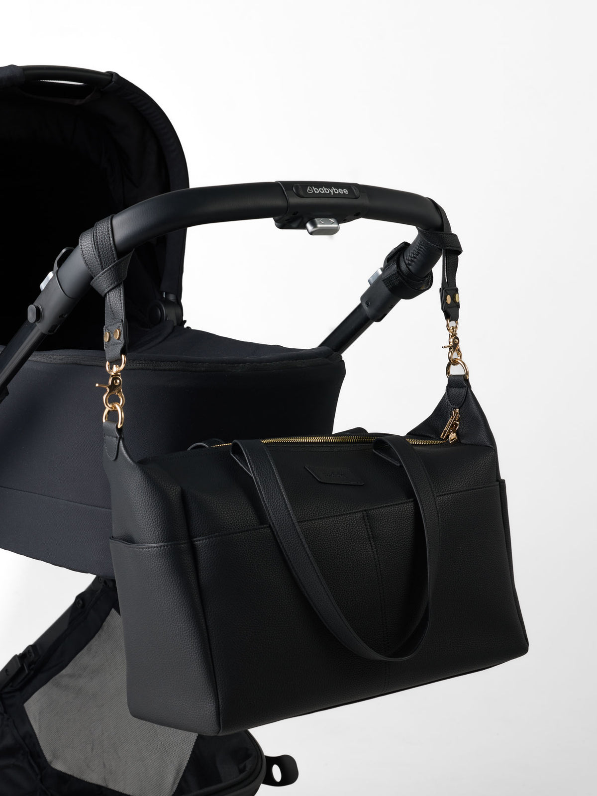Sable Bebe black vegan leather nappy bag hanging on a black pram by two pram straps