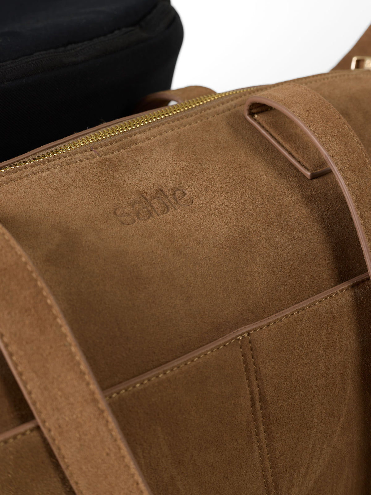 Close-up image of our suede nappy bag attached to a stroller handle with gold hardware and debossed sable logo - Sable Bebe