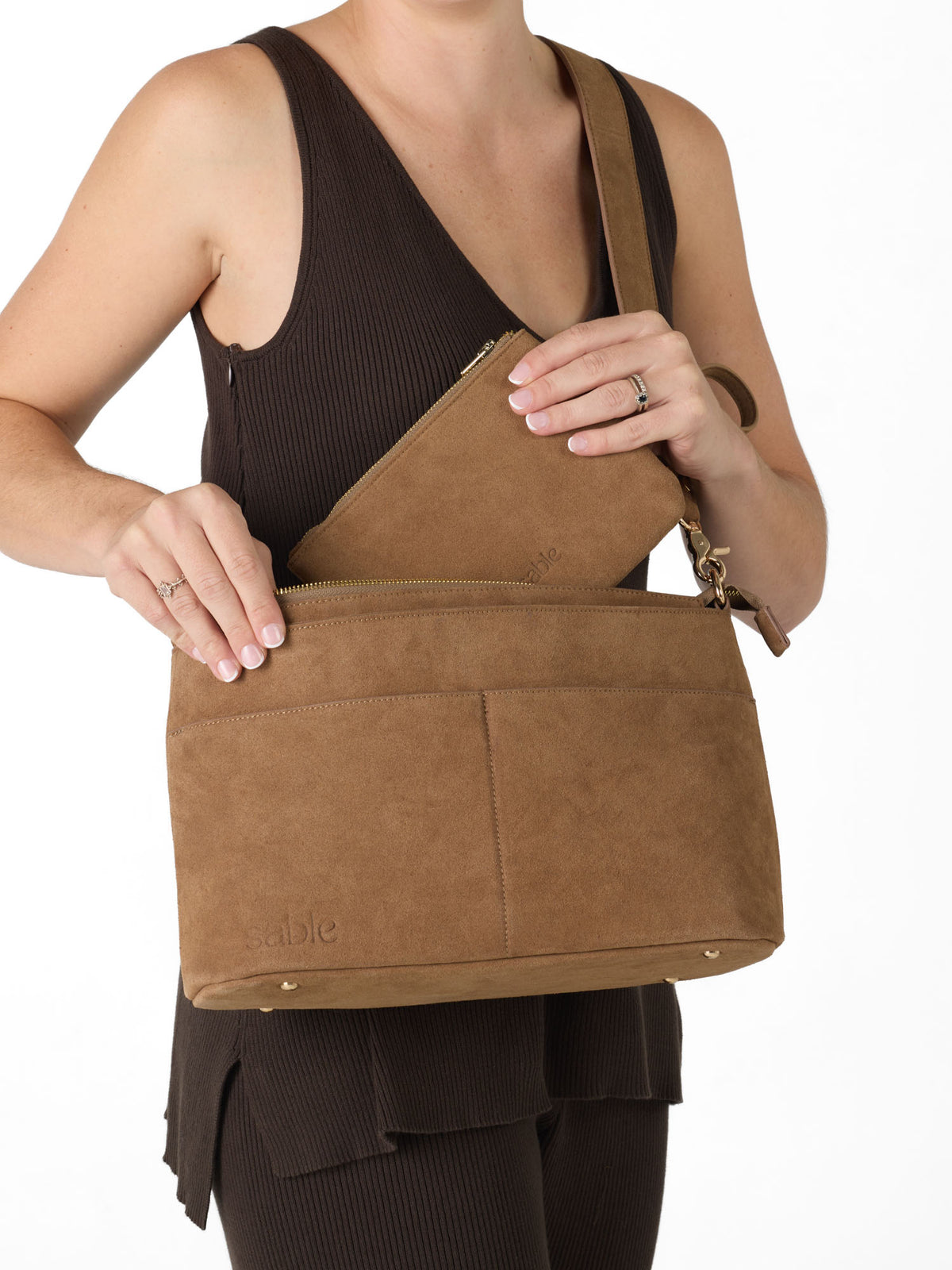 Mother wearing her suede pram caddy crossbody bag and putting in her suede zipped pouch - Sable Bebe