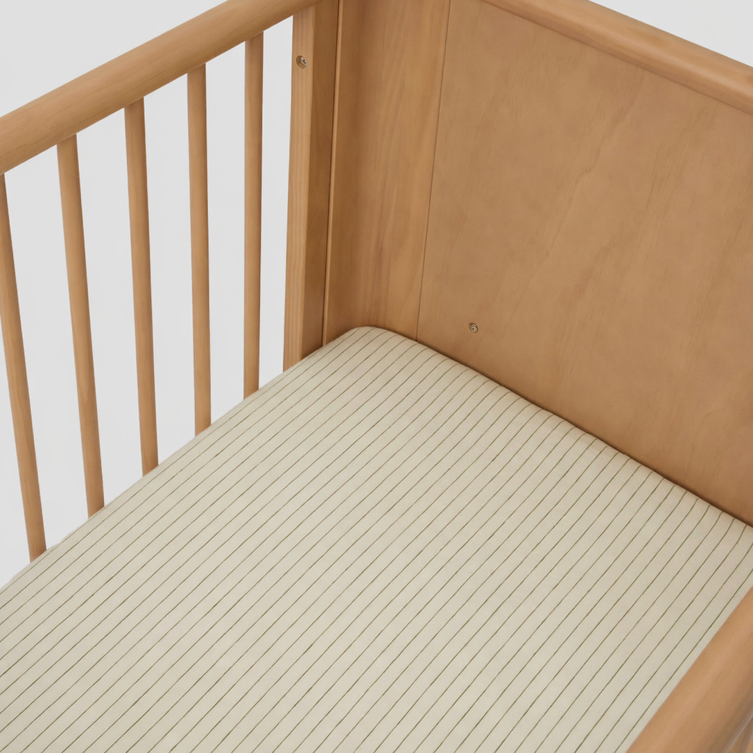 Olive Pencil Striped Linen Cot Sheet styled in a nursery setting made from breathable 100% pure linen