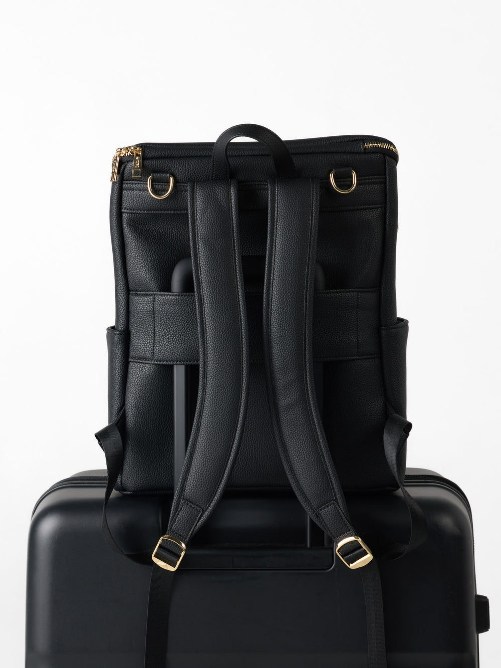 Black nappy backpack on a suitcase handle via its luggage sleeve