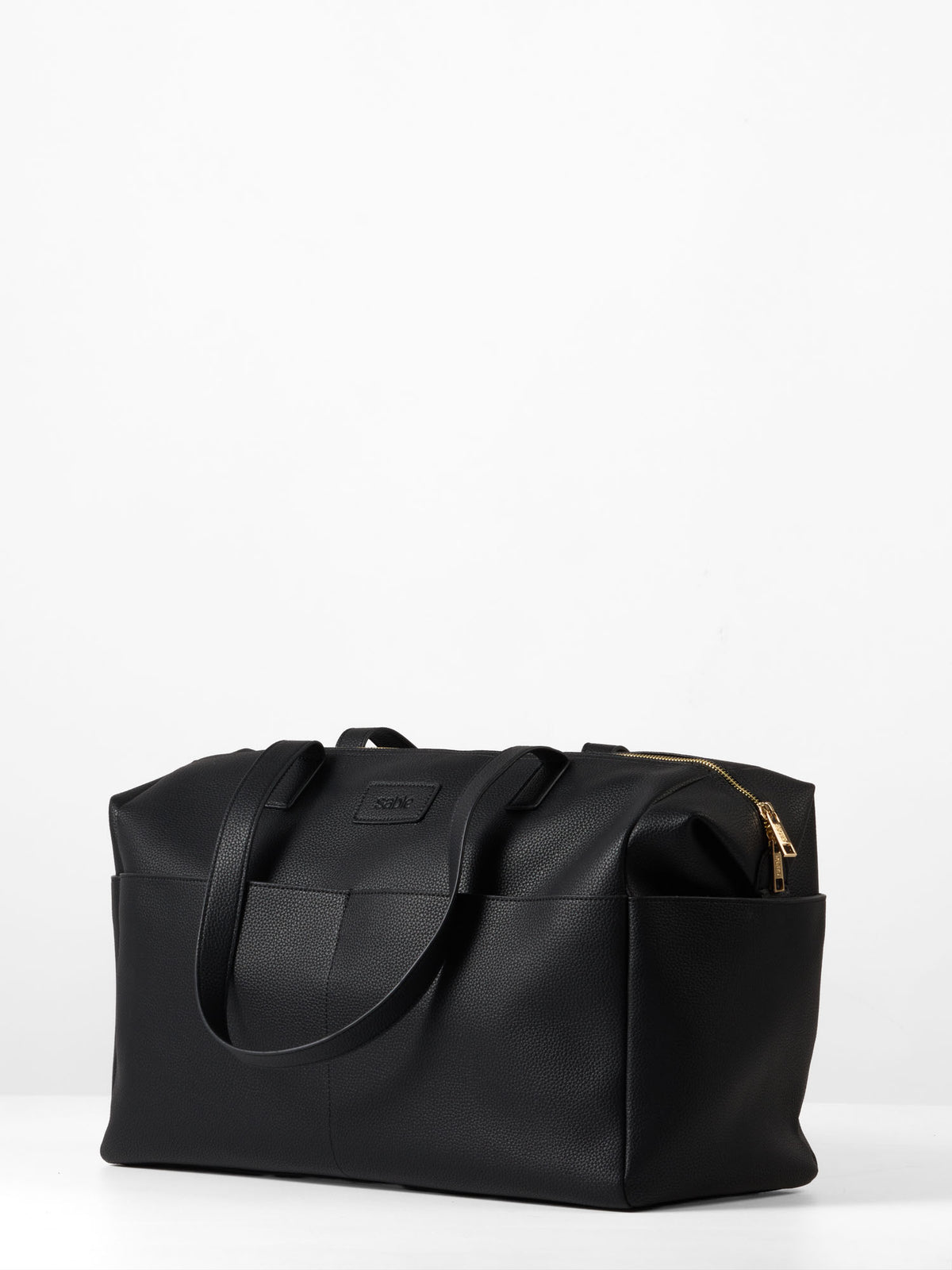 Side view image of the black vegan leather nappy bag displaying the side slip pocket and gold hardware
