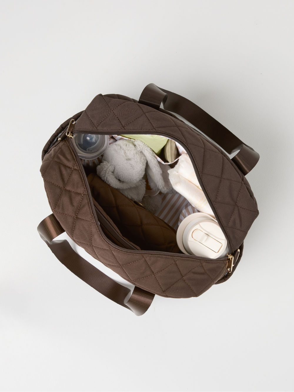 Top view of the open chocolate quilted nappy bag packed with bottles and a soft toy