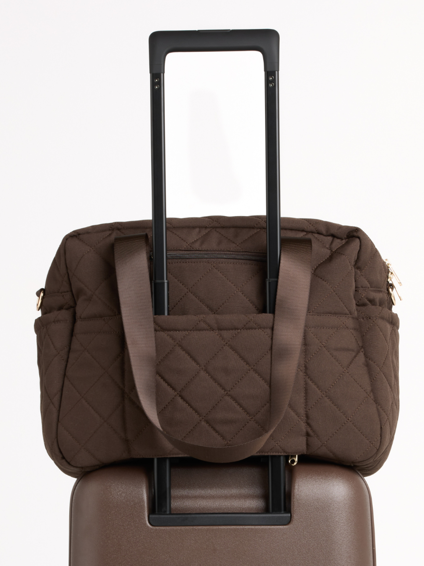 Chocolate quilted nappy bag on a suitcase, held by its luggage sleeve