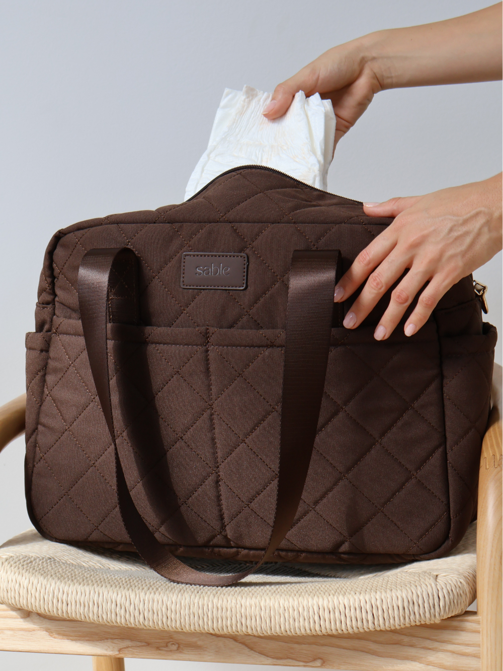 Nappies being packed into the chocolate quilted nappy bag on a chair
