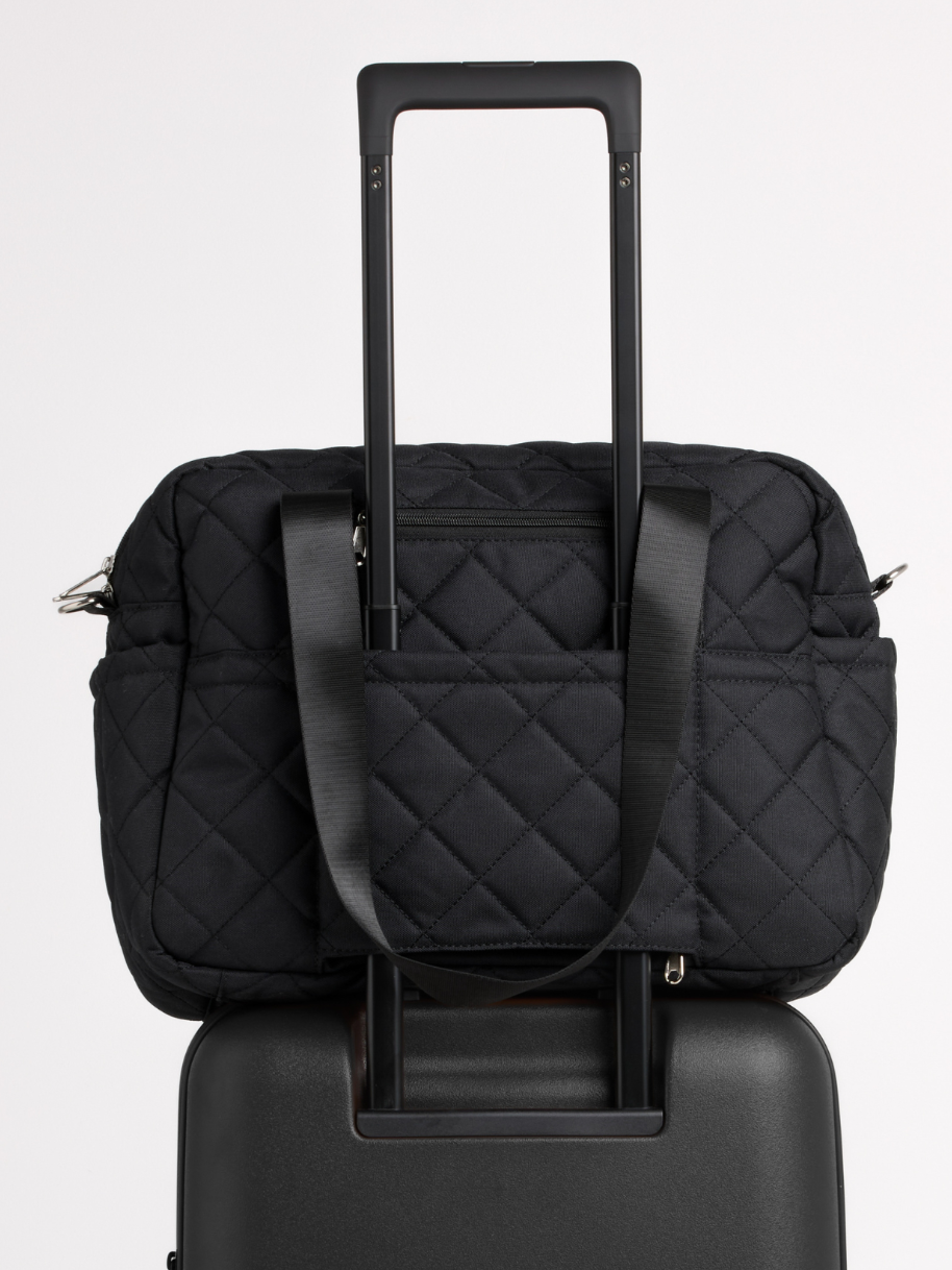Black quilted nappy bag on a suitcase, held by its luggage sleeve