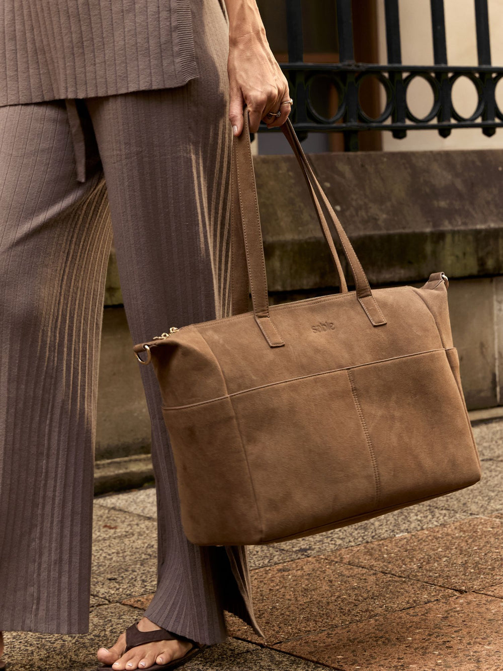 Woman carrying the brown suede nappy bag by its handles on a city street