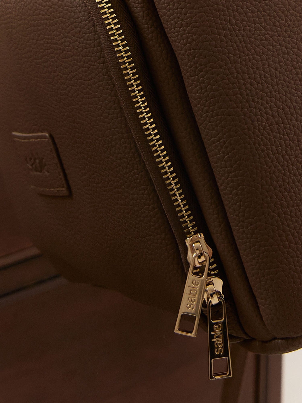 Close-up of a brown leather bag with a zipper and visible brand logo.