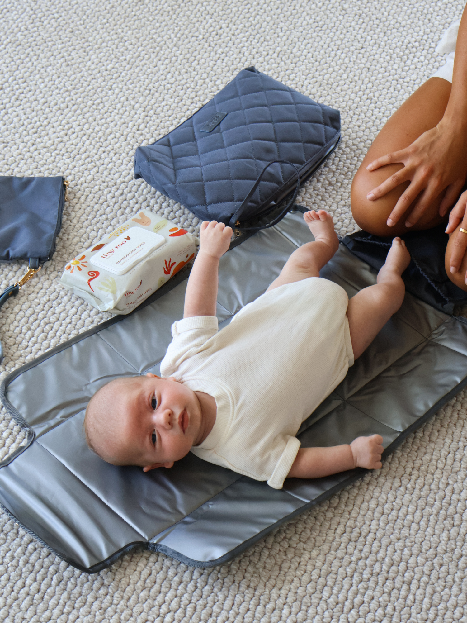 Baby lying on a changing pad with a diaper bag and wipes nearby