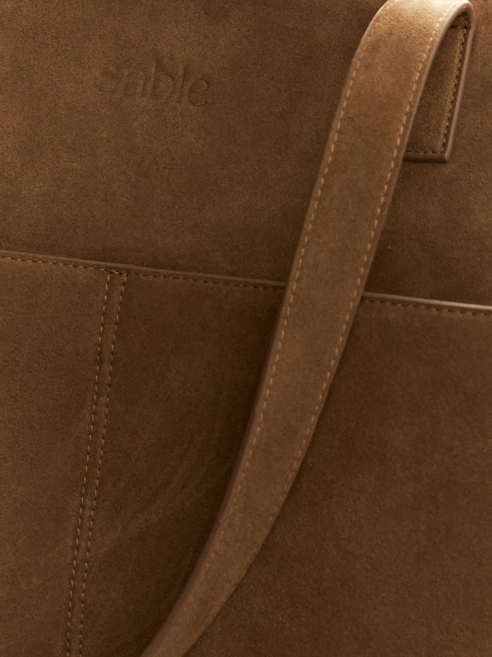 Close-up of brown suede texture with the shoulder strap and debossed logo