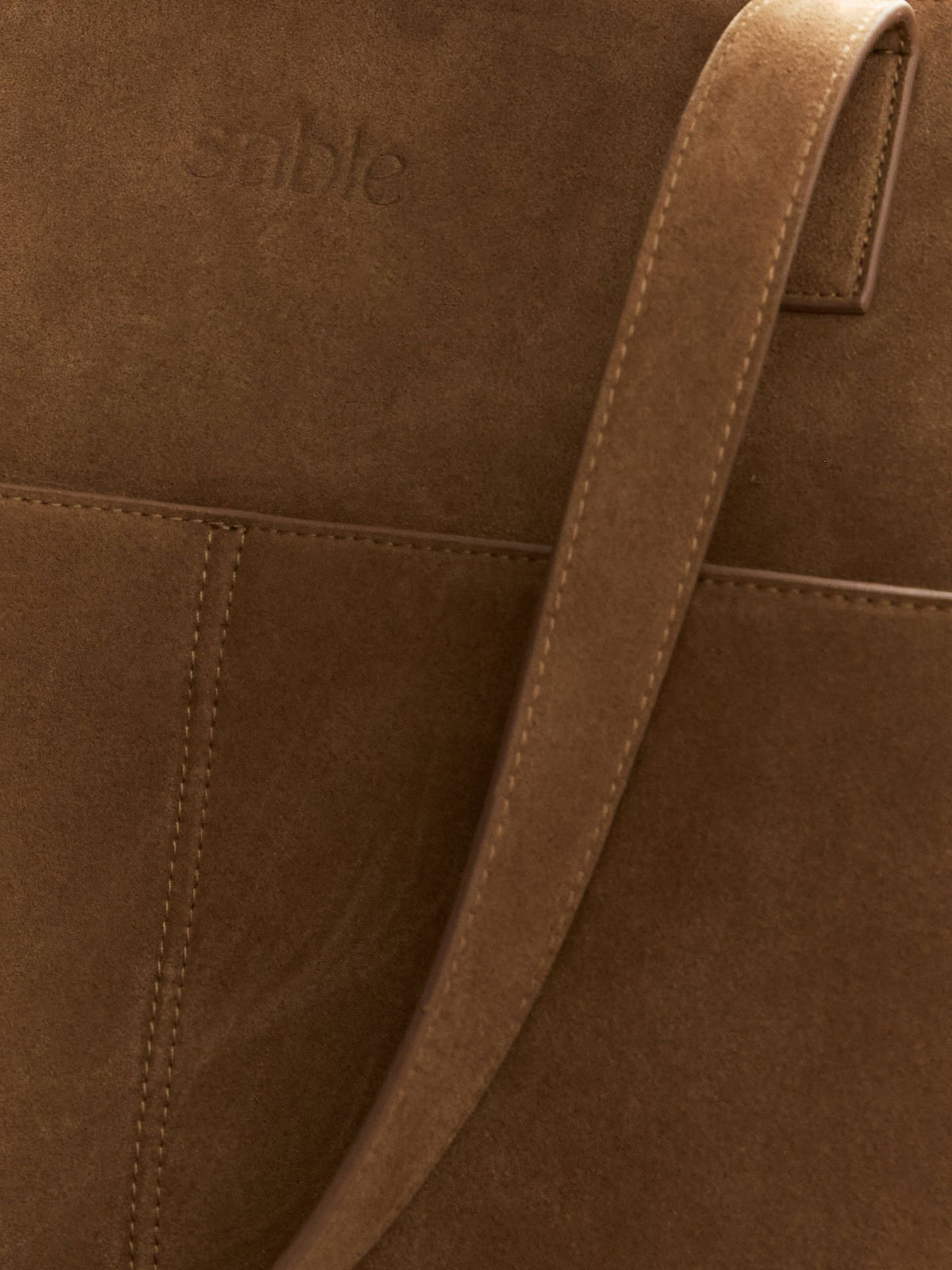 Close-up of a brown suede or leather bag with a matching shoulder strap and a faint embossed brand name that appears to read Sable Bebe